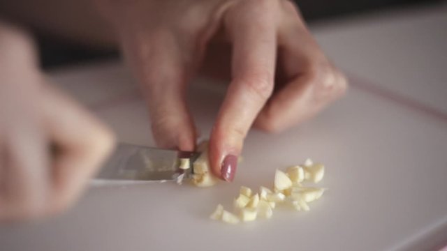 Young woman's hands cut fresh garlic head on white background