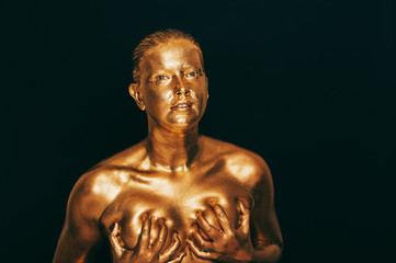 Portrait of sensual woman covered with golden paint, posing on black background, eyes closed