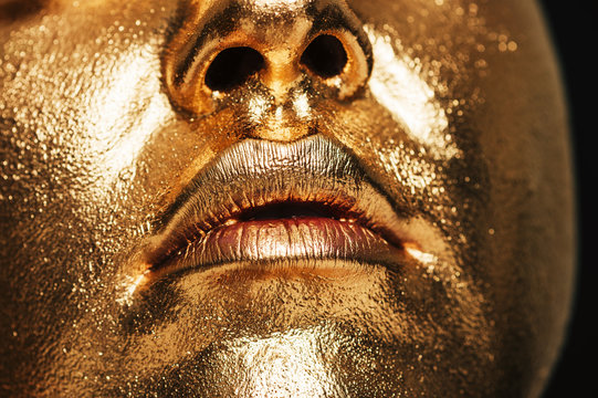 Close up image of woman face covered with golden paint