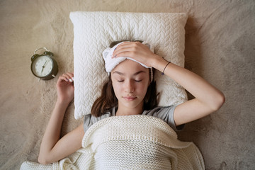 Sleepy teenager girl turning alarm off in the morning while lying in bed 