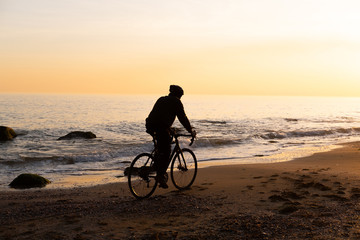 Fototapeta premium silhouette of young male bicycle rider in helmet on the beach during beautiful sunset