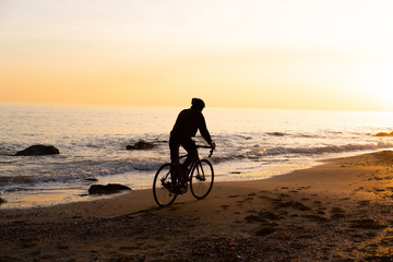 Obraz premium silhouette of young male bicycle rider in helmet on the beach during beautiful sunset 