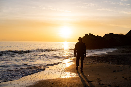 silhouette of male traveler stand near cliff and watch beautiful sunset in the sea