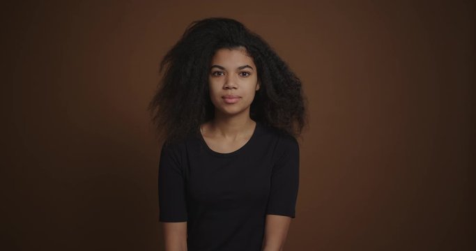 Portrait of young african american girl emotionally looking to camera at brown background