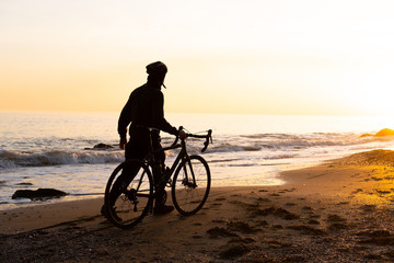 Fototapeta premium silhouette of young male bicycle rider in helmet on the beach during beautiful sunset