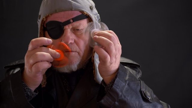 Portrait of strange elderly man spinning spiner on his nose. fancy pensioner with gray beard and black blindfold. bizarre people. 4K. Soothing toy. Autism. Senile memory loss, falling into childhood