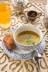 chicken broth with bread bun and parsley in bowl with glass of yellow drink on oriental wooden table