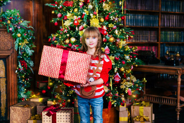 Beautiful blonde girl stands at the Christmas tree with gifts. Holidays, sale concept.