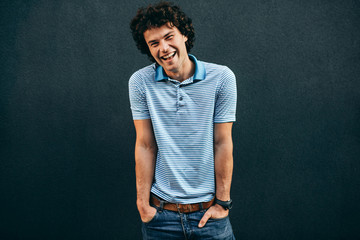 Handsome positive young man posing for advertisement, smiling and looking at the camera, standing at building gray wall outdoors. Happy smart student male has positive expression. People and emotion