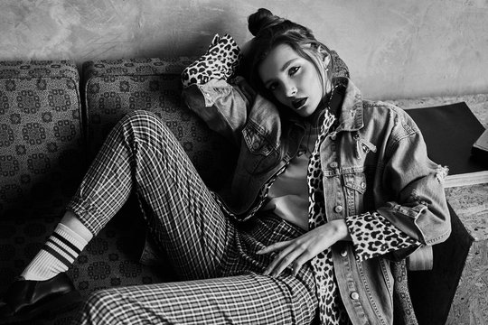 Black-white portrait of a sexy girl in grunge style. Dramatic black and white photo of a beautiful woman on a dark background. Female model in Denim jacket, plaid pants, white socks and leopard shoes.