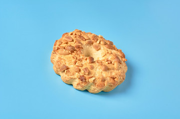 Single fresh circle oat cookie with hole and peanuts lies on blue desk on kitchen. Close-up