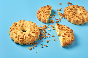 Whole and halves of fresh circle oat cookies with peanuts and crumbs lies on blue desk on kitchen. Close-up