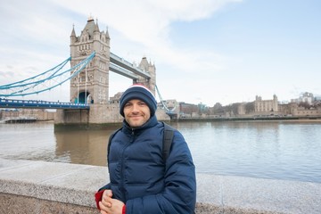 Portrait of mid adult man in warm clothing standing in front of tower bridge; London; UK