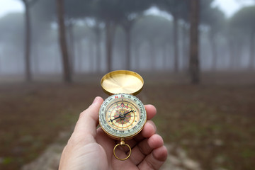 A person lost in nature tries to orient himself with a compass in a forest with fog
