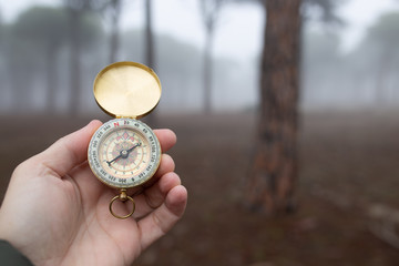 A person lost in nature tries to orient himself with a compass in a forest with fog