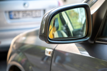 Close up of rearview mirror of a car parked near curb on the side of the street on a parking lot.