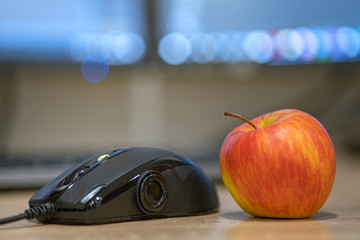 Computer mouse and a red apple on blurred background of light screen.