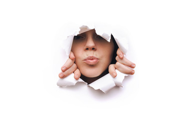 Portrait of a young caucasian woman looking through the hole in white paper. The concept of kiss, harassment, seduction and flirting.