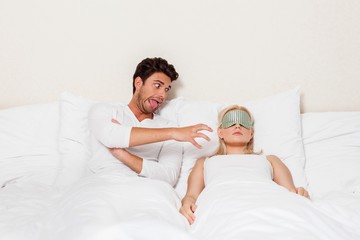 Fototapeta premium Angry young man teasing sleeping woman in bed