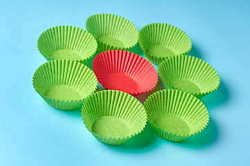 Red and green paper molds for baking muffins in form of flower lies on blue desk on kitchen. Close-up
