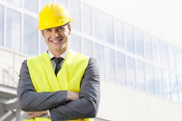 Portrait of smiling young male architect standing arms crossed outside office building