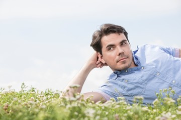 Thoughtful man lying on grass against sky