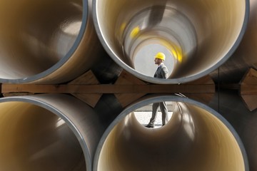 Full length side view of young male architect walking by stacked pipes at construction site
