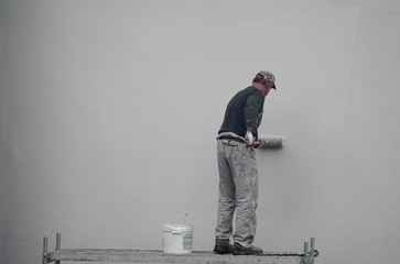 a male painter paints the wall with a roller blue paint. outdoor work in an apartment building and multi-storey building.