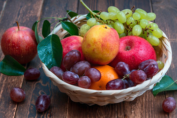 red grape berries and fresh fruits in a straw basket on a dark wooden background.