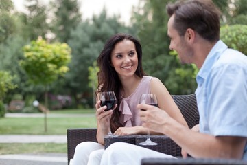 Happy young couple having red wine on chairs in park