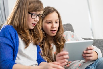 Shocked sisters using digital tablet on sofa at home