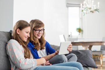 Happy sisters using digital tablet on sofa at home