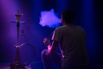 The man Smoking the classic Shisha. Beautiful background, with colored rays of light and smoke. The concept of hookah Smoking.