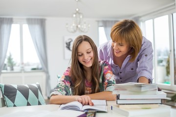 Smiling mother assisting daughter in doing homework at table