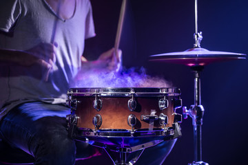A drummer plays drums on a blue background. Beautiful special effects of light and smoke. The process of playing a musical instrument.