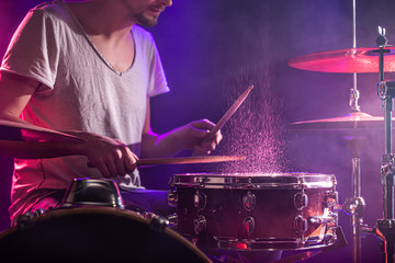 Fototapeta na wymiar The drummer plays the drums. Beautiful blue and red background, with rays of light. Beautiful special effects smoke and lighting. The process of playing a musical instrument. Close-up photo.