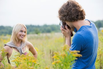 Young man photographing girlfriend in field