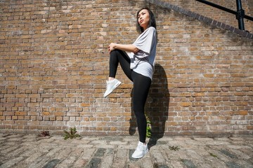 Full length side view of young fit woman stretching against brick wall