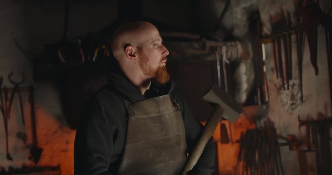 Portrait of young blacksmith with big hammer in workshop dark eerie