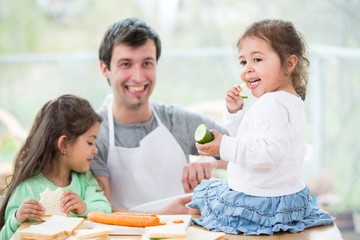 Happy father preparing sandwiches while daughters eating at home