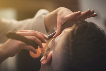 Barber with a dangerous razor shaves a bearded man in a barbershop