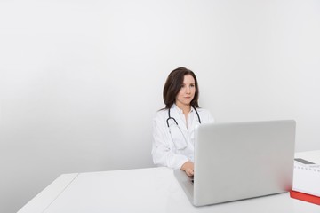 Young female doctor looking away while using laptop at desk in clinic
