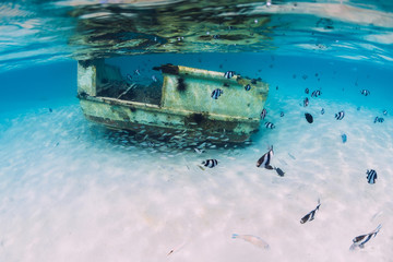 Tropical ocean with wreck of boat on sandy bottom, underwater