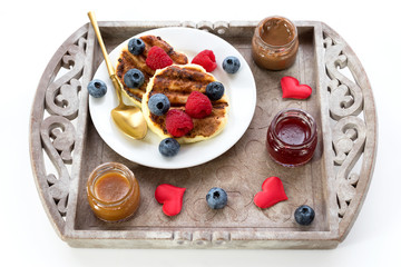 Curd cheese cakes on a vintage tray with different sauces and hearts for Valentine's Day holiday for breakfast.