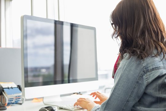 Rear view of businesswoman using desktop computer in creative office