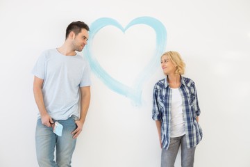 Mid-adult couple looking at each other with painted heart on wall