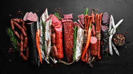 Assortment of sausages, salami and fuet. Dried and smoked salami on black wooden background. Top...