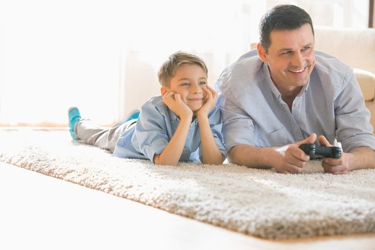 Happy father and son playing video game on floor at home