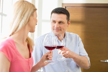 Couple toasting red wine glasses in kitchen