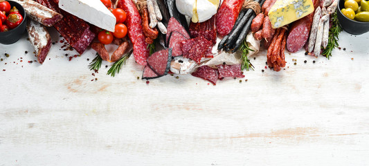 Assortment of cheese, dried salami and smoked sausages on a white wooden background. Top view. Free...